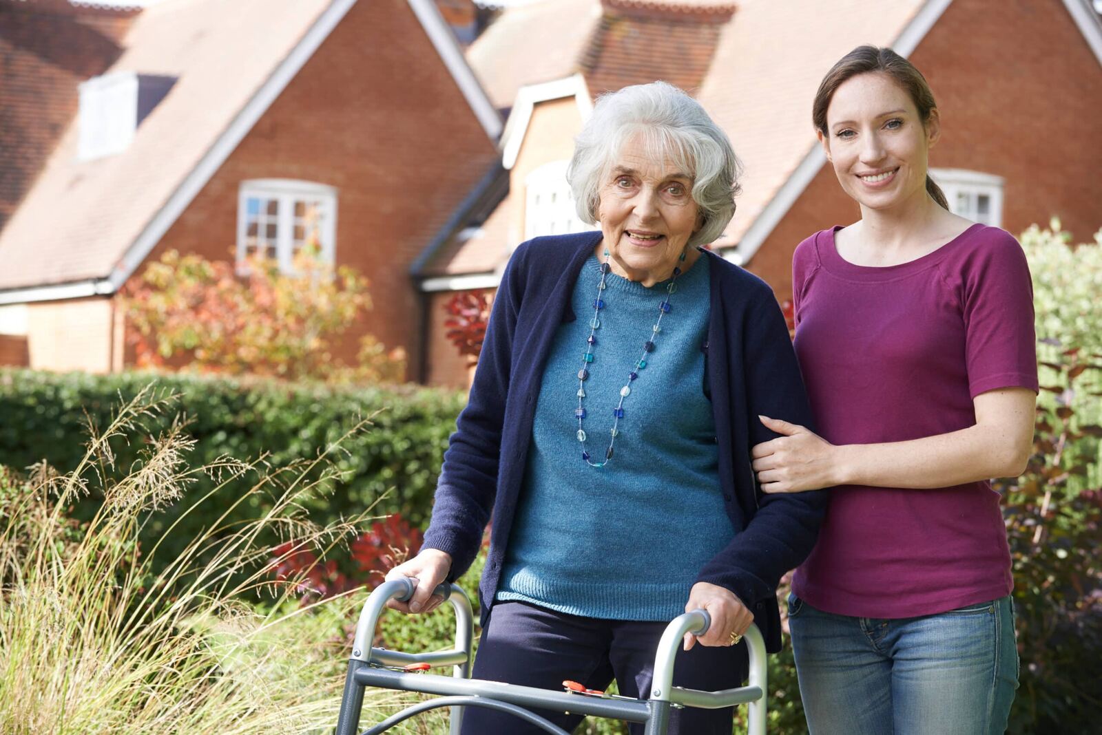 A carer walking arm in arm with an older lady outside her home